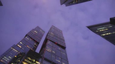Timelaps. Camdan yapılmış olağandışı şeklin modern gökdelenler. Alt görünüm. Günbatımı