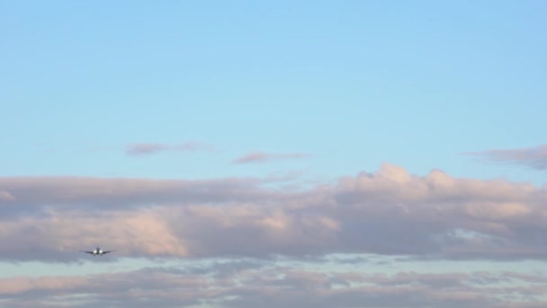 Avión de pasajeros volando contra el cielo azul a través de las nubes naranja y púrpura — Vídeos de Stock