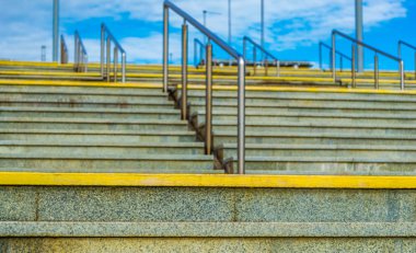 Cennete giden modern granit merdivenler. Arka planda mavi bir gökyüzü ve beyaz bulutlar var. Çelik korkuluklar. Berrak, güneşli hava.