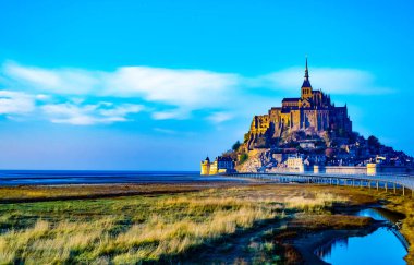 Mont Saint Michel, Fransa güzel ortaçağ kalesi. Adada bulunan manastır, surlarla çevrilidir. Köprü adaya gidiyor. Güzel mavi gökyüzü ve kabarık beyaz bulutlar. Gündüz