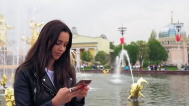 Sevimli kız gülümsüyor ve akıllı telefon bir mesaj yazın. Şık kıyafetler, siyah ceket