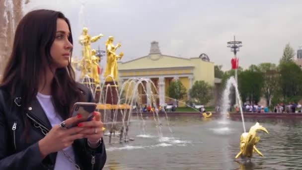 Menina bonito com belos olhos azuis, em roupas da moda, usando um telefone celular — Vídeo de Stock