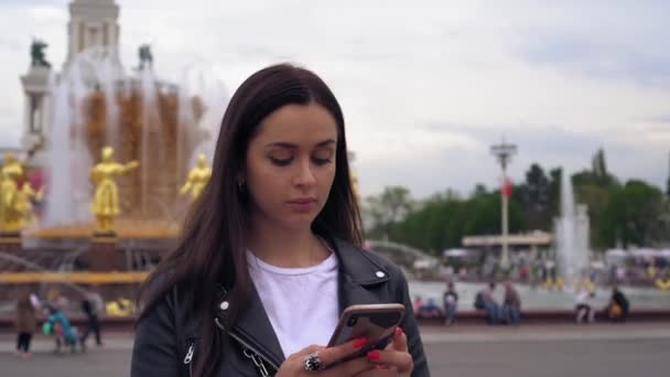 Menina atraente, elegante, em uma jaqueta preta, usando um telefone celular . — Vídeo de Stock