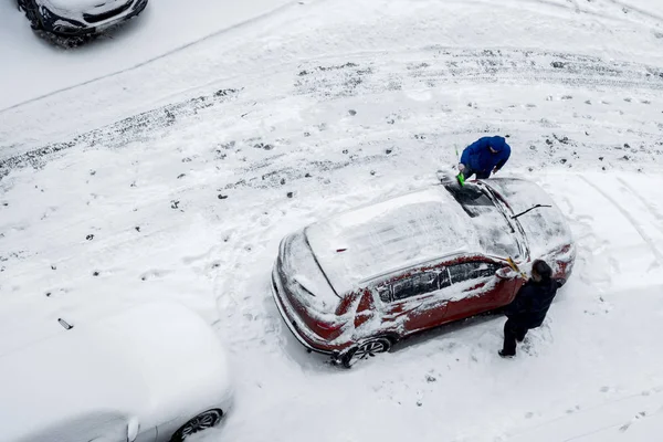 Dois homens, com pincéis, removem a neve do carro. Vista superior, aeria — Fotografia de Stock