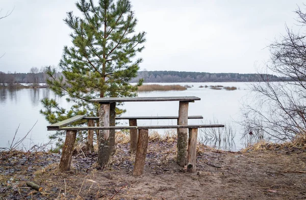 Meja kayu untuk rekreasi luar ruangan di tepi sungai pada musim semi, menunggu pengunjung . — Stok Foto