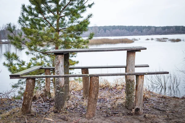 Mesa de madera para la recreación al aire libre en la orilla del río en primavera en marzo, esperando a los visitantes . — Foto de Stock