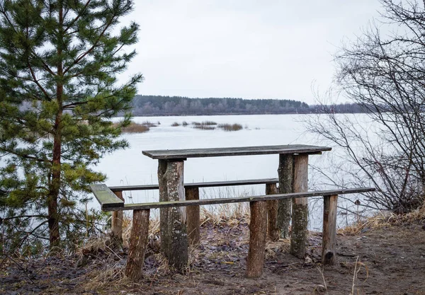 Meja kayu untuk rekreasi luar ruangan di tepi sungai pada musim semi, menunggu pengunjung . — Stok Foto