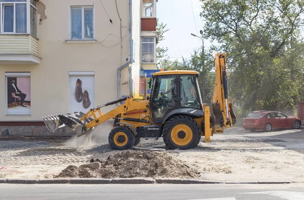 Orange excavator on wheels works in the city