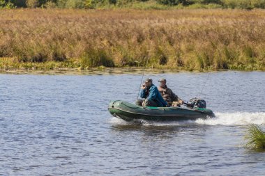 Anglers güneşli bir yaz gününde balık arayan bir nehir üzerinde motorboat gitmek
