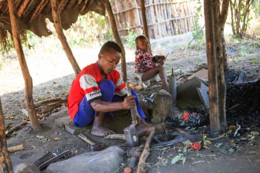 Ari Köyü, Jinka, Omo Nehri Vadisi, Etiyopya - Ocak, 2018. Çekiç ve Hatıra Eşyası turistler için oluşturma demirci çocuk. Küçük kardeşim arka plan üzerinde oturan