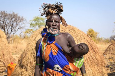 Jinka, Omo Nehri Vadisi, Etiyopya - Ocak, 2018. Mursi kabile kadın emzirme onu kulübe önünde duran çocuğu,