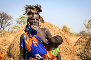 Jinka, Omo Nehri Vadisi, Etiyopya - Ocak, 2018. Mursi kabile kadın emzirme onu kulübe önünde duran çocuğu,
