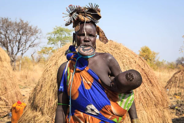 Jinka, Omo Nehri Vadisi, Etiyopya - Ocak, 2018. Mursi kabile kadın emzirme onu kulübe önünde duran çocuğu,
