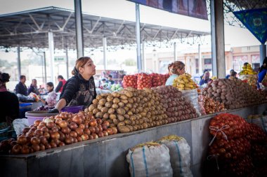 Semerkand, Özbekistan, Ekim, 2016: Kadın satan patates ve soğan şehrin ana Market (bazaar) müşteriler için bekliyor. Onun mal büyük yığınları ile çevrili