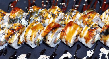 Yılan balığı suşi plastik kutu ambalaj tepsisinde siyah taş arduvaz arka plan üzerine alır.