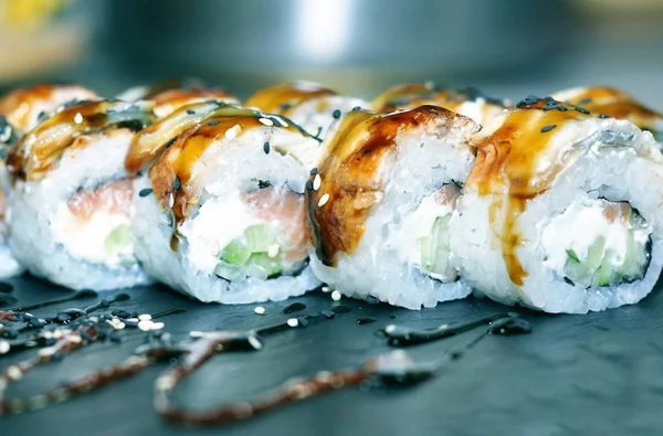 Yılan balığı suşi plastik kutu ambalaj tepsisinde siyah taş arduvaz arka plan üzerine alır.