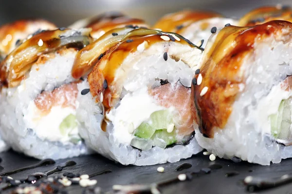 Yılan balığı suşi plastik kutu ambalaj tepsisinde siyah taş arduvaz arka plan üzerine alır.