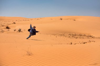 Avrupa görünüm eğlenceli bir çocuk kumullar çalışır. Oğlan mavi kot pantolon ve mavi bir ceket giyiyor. Güneşli bir bahar günü. Parlak duygu.
