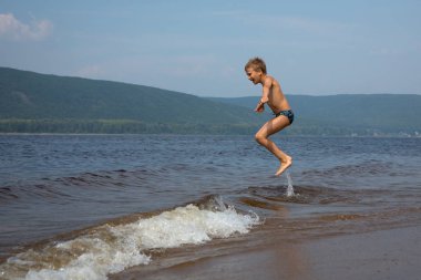 Çocuk sahilde dalgaların atlar. Güneşli yaz gün. 