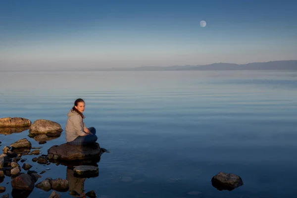 Тихий закат над рекой. Девушка сидит на большом камне . — стоковое фото