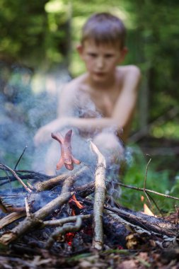 Çocuk ateşte sosis kızartmak. Ormanda çocuk. 