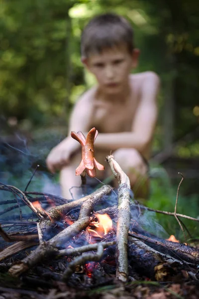 Çocuk ateşte sosis kızartmak. Ormanda çocuk. 