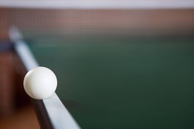 Yeşil bir ping pong masasının kenarında bir ping pong topu. 