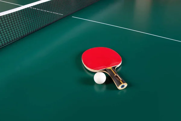 乒乓球球拍和绿色桌子上的一个球。乒乓球网. — 图库照片
