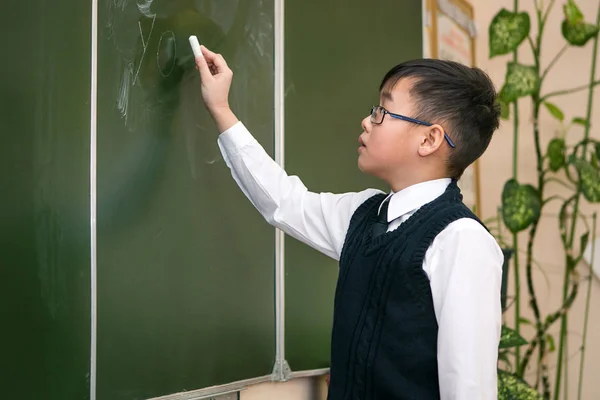 Мальчик азиатского происхождения пишет в школьном совете. The bo — стоковое фото