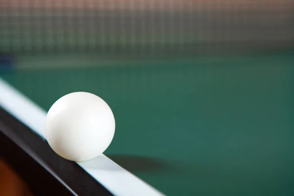A ping pong ball on the edge of a green ping pong table. Close-u