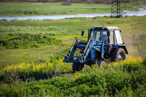 Trator cavalga no campo. Dia ensolarado de verão. Colza em flor. Ru... — Fotografia de Stock