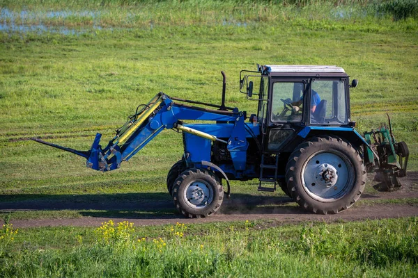 Egy traktor a réten egy út mentén vezetés. Nyári napsütéses nap. Orosz provincia. — Stock Fotó