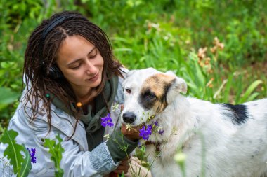 Kulaklıklı kız bir köpeğe sarılır. Beyaz bir rüzgarlık giyen dreadlocks ile görünüm Latino kız. Hayvanlarla iletişim kurmanın neşesi ve zevki.