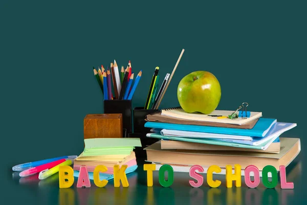 Inscriptie terug naar school. Stilleven met schoolbenodigdheden. Groene achtergrond. Notebooks, notebooks, viltstiften, gekleurde potloden, een appel. Kleurrijke foto. — Stockfoto