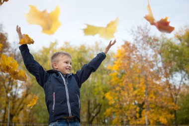 Çocuk sonbahar yaprakları atıyor. Neşeli çocuk. Park, sonbahar günü.