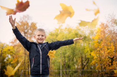 Çocuk sonbahar yaprakları atıyor. Neşeli çocuk. Park, sonbahar günü.