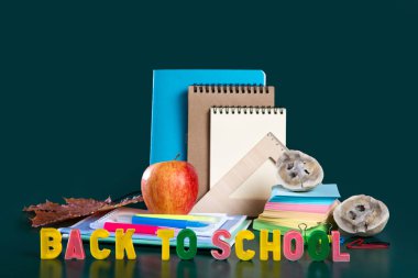 Okula geri yazıt. Okul malzemeleriyle dolu bir hayat. Yeşil arka plan. Defterler, defterler, keçeli kalemler, renkli kalemler, elma. Renkli resim.