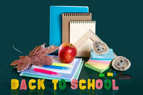 Inscriptie terug naar school. Stilleven met schoolbenodigdheden. Groene achtergrond. Notebooks, notebooks, viltstiften, gekleurde potloden, een appel. Kleurrijke foto. — Stockfoto