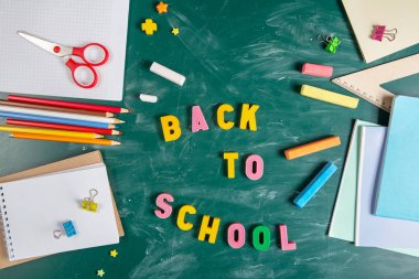 Okul malzemeleriyle natürmort. Kara tahta tebeşir lezbeşi. Yeşil arka plan. Defterler, defterler, keçeli kalemler, renkli kalemler. Renkli resim. Öğretim yılı başında.