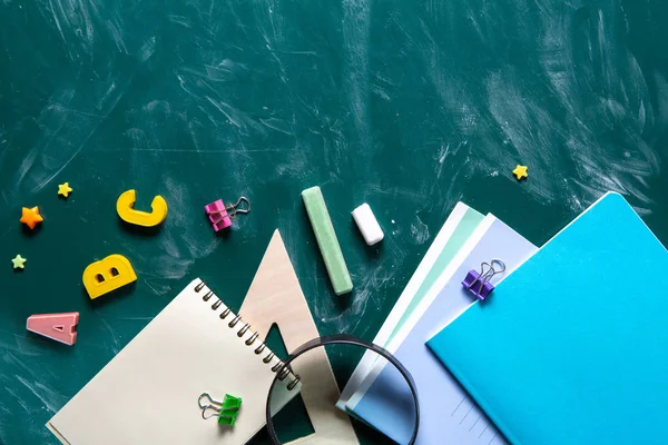 Bodegón con útiles escolares. Pizarra en pizarra de tiza. Fondo verde. Cuadernos, cuadernos, rotuladores, lápices de colores . —  Fotos de Stock