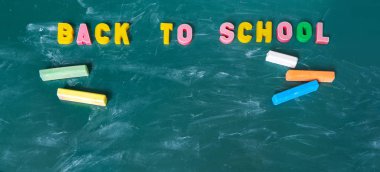 Afiş. Okula geri yazıt. Okul malzemeleriyle natürmort. Çok renkli tebeşir. Kara tahta tebeşir lezbeşi. Yeşil arka plan. Öğretim yılı başında.