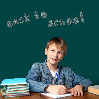 Okul tahtasında yazıt. Avrupa görünümü bir çocuk okul yeşil tahta arka planda oturuyor. Bir genç bir defter yazıyor. 