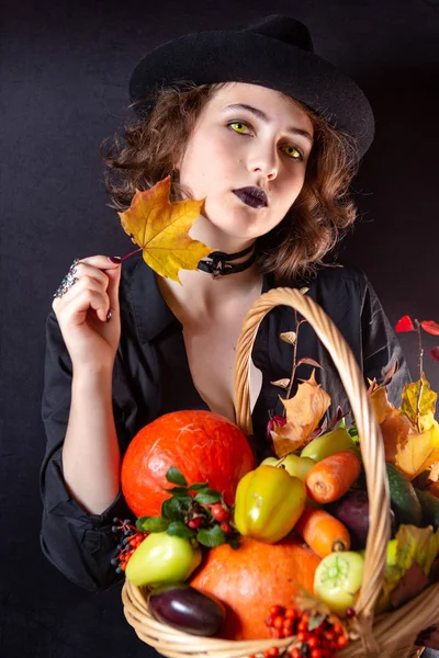 Dívka oblečená v černém na černém pozadí s košíkem zeleniny. Halloween kostým. — Stock fotografie