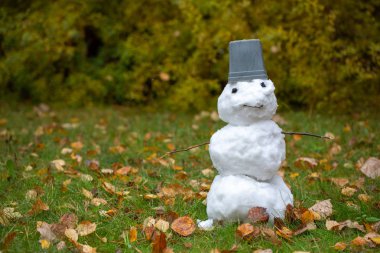 İlk kardan gelen komik kardan adam. Çimlerde sonbahar yaprakları. Sarı bulanık arkaplan. 