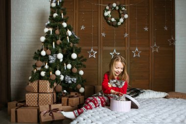 Kırmızı pijamalı bir kız sevimli kedilerle yatakta oturuyor. Parlak duygu. Noel ağacının altında hediyeler.