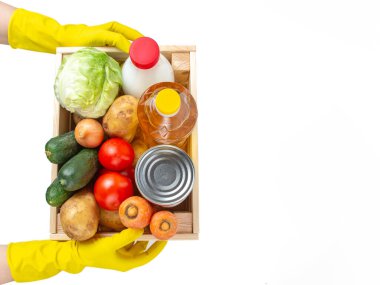 Kurye, beyaz izole edilmiş arka planda içi yiyecek dolu ahşap bir kutu tutuyor. Taze sebze, konserve yiyecek, sebze yağı ve süt bir kutuda. Tarım ürünleri. Ürünlerin teslimatı. Eldivenli eller. 