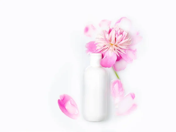 Jars of cream and pink peony in a milk bath. Conceptual photo: the best cosmetic tool for body and face care. Gentle care. Copy space, flat lay. Natural cosmetics, mock up.