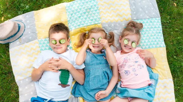 Kids have fun at summer camp during the holidays. Ideas for fun activities in the summer. Children play on a patchwork rug. Kids put pieces of cucumber over their eyes