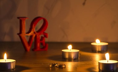 İki yüzük ve mum soldaki beyaz zemin üzerine kırmızı aşk mektupları