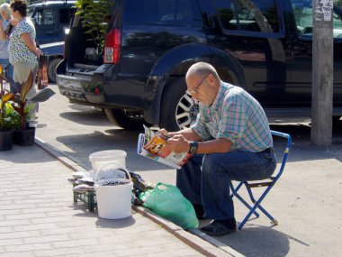 Uglich, Rusya - 5 Ağustos 2017: Bir sokak pazarında dergi okuyan, katlanan bir taburede oturan, aile çiftliğinden yaşlı bir ürün satıcısı 